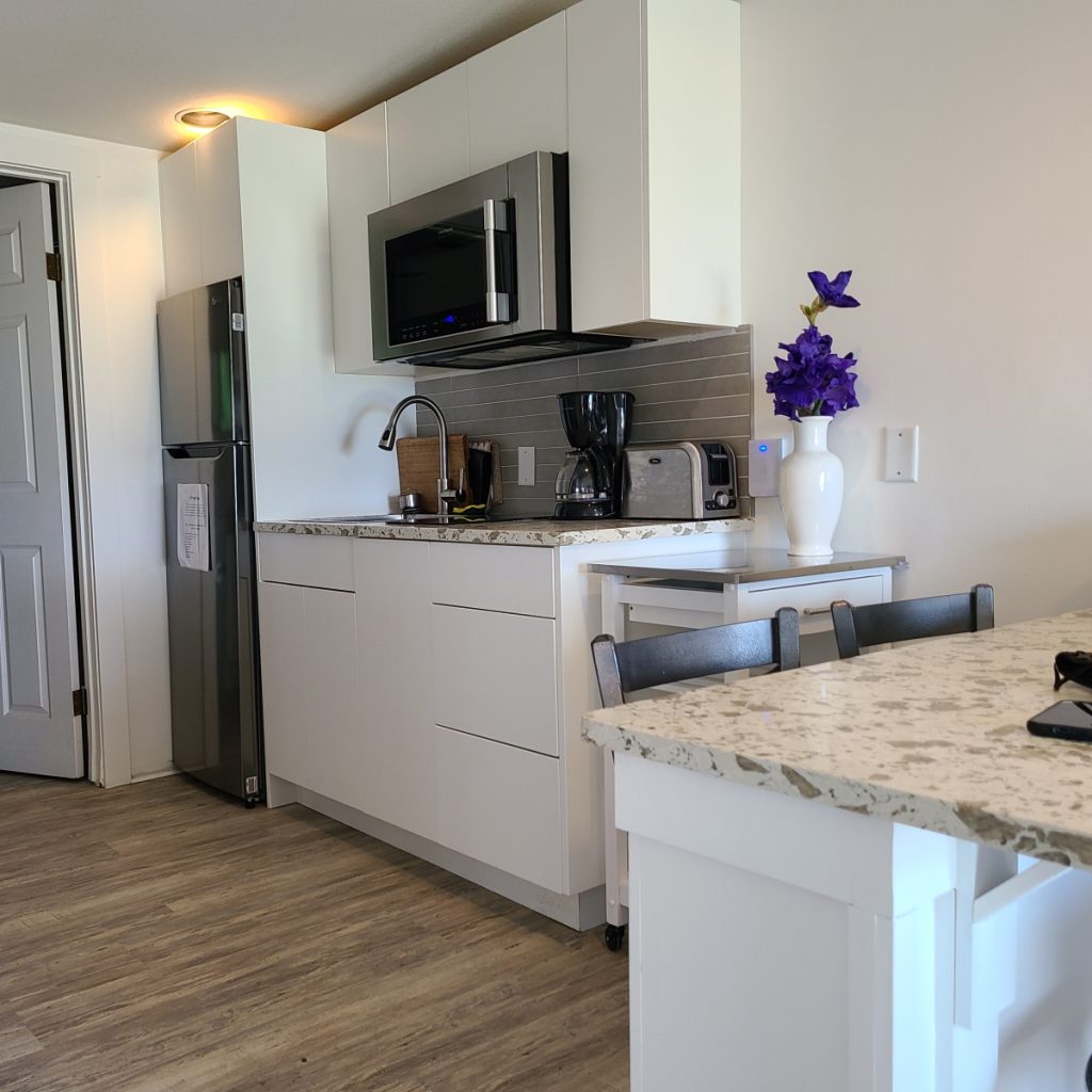 Modern kitchen in 2-bedroom beachfront suite at Qualicum Breeze Resort, featuring stainless steel appliances, granite countertops, coffee maker, and decorative flowers, ideal for family accommodations.