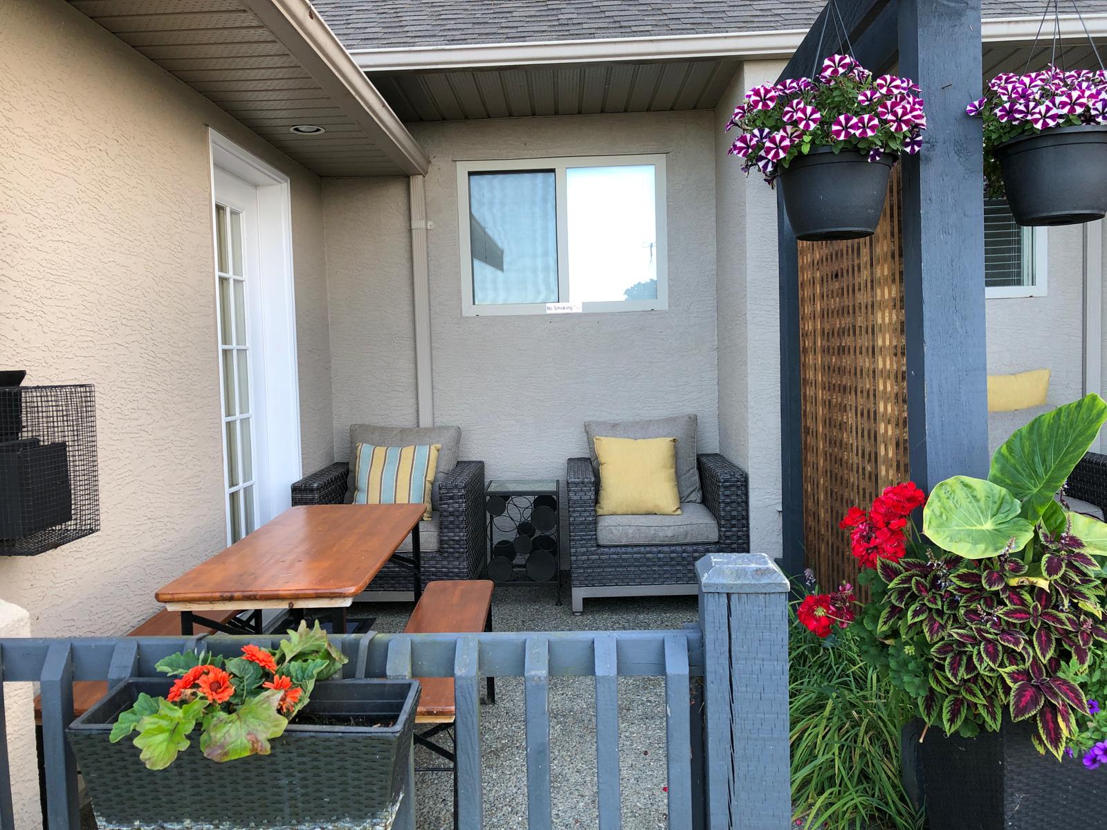 Beachfront patio area of a 2-bedroom suite at Qualicum Breeze Resort, featuring comfortable seating, a wooden table, and vibrant flower pots, ideal for family relaxation.
